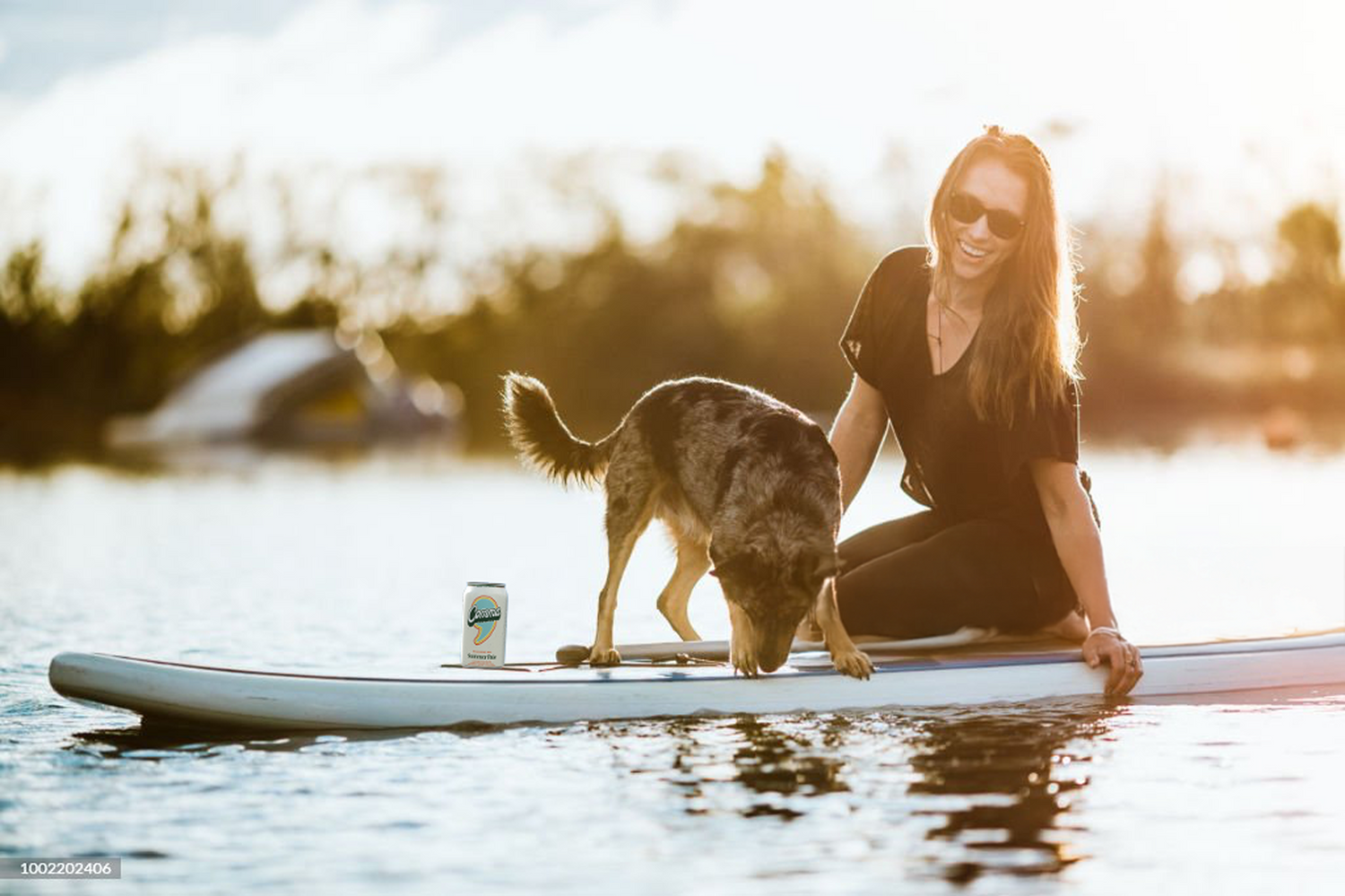 A woman on kneeling on her paddle board with her dog and a Comma